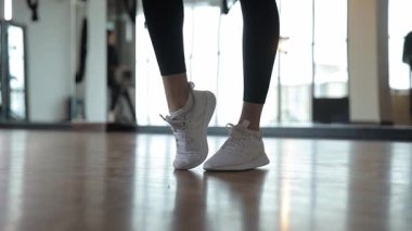 Beyaz spor ayakkabılı bir kadının dinamik bir fotoğrafı, spor salonunun ve modern spor salonunun özünü gözler önüne seriyor..