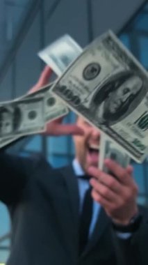 Şık takım elbiseli neşeli bir adam, büyük başarıyı ve etkileyici finansal başarıyı simgeleyen nakit atıyor..