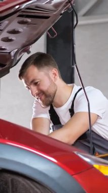 Yetenekli bir tamirci, kırmızı bir arabanın motorunu dikkatle inceler. Hem ustalığını hem de kendini işine adadığını gösterir..