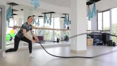 Parlak ve ferah bir fitness stüdyosunda, bir kadın savaş halatları kullanarak yoğun bir idmana girişir.