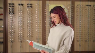 Genç bir kadın moda ve modaya uygun bir optik dükkanında çeşitli göz giysisi seçeneklerini inceliyor..