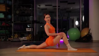 Atletik bir kız tam bir bölünme sergileyerek atletizm ve esnekliğini gösteriyor. Modern bir spor salonunda..