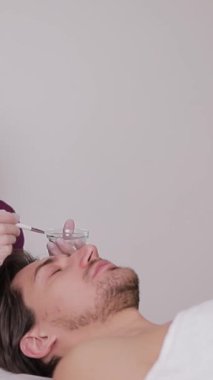 Profesyonel bir kozmetik uzmanının erkek müşterilere estetik işlemler uyguladığı dikey bir video..