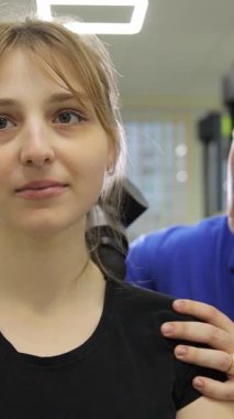  Dikey bir video perküsyon masajcısı kullanan bir kadına boyun terapisi uygulayan etkili kas gevşemesi ve rehabilitasyona odaklanan bir terapisti yakalar..