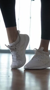 Bir kadının beyaz spor ayakkabılarını, vücut geliştiren fitness ve beden kültürünü vurgulayan dinamik bir çekim. Dikey video.