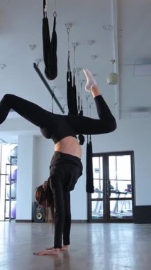 Genç bir kadın, aynalı bir stüdyoda havanın ortasında çarpıcı bir yoga pozu veriyor. Dikey video.