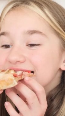 Neşeli bir çocuk lezzetli bir dilim pizzanın tadını çıkarırken tasasız yemeğin özünü mükemmel bir şekilde yakalıyor.