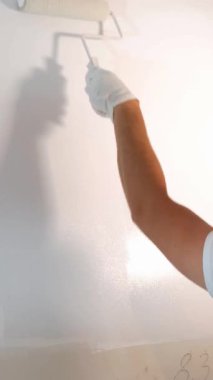 Temiz beyaz bir duvar boyamak için silindiri kullanan bir el, ev dekorasyonunun ve DIY 'in özünü yakalıyor.