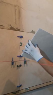 Yetenekli bir profesyonel tiler, duvardaki fayansları titizlikle ayarlar. Boşlukları kullanarak, tam ve doğru uyumu sağlar..