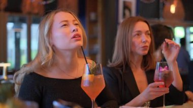 İki kadın modaya uygun, şık bir barda canlı kokteyller içiyor. Arkadaşlıklarını, zevklerini ve eğlencelerini ön plana çıkarıyorlar.
