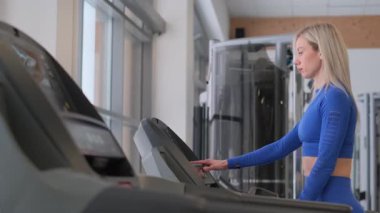 Şık ve sağlıklı bir kadın modern bir spor salonundaki koşu bandıyla güçlü bir şekilde çarpışır.