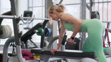 Formda ve sağlıklı bir kadın şık ve modern bir spor salonunda halterle aktif olarak egzersiz yapıyor.