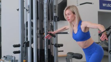 Kendini işine adamış ve odaklanmış bir kadın spor salonundaki bir kablo makinesinde yoğun bir egzersiz yapıyor.