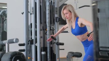 Odaklanmış bir kadın, modern bir spor salonunda, günlük yaşamda sağlık ve zindeliği ön plana çıkaran bir güç eğitimiyle meşgul..