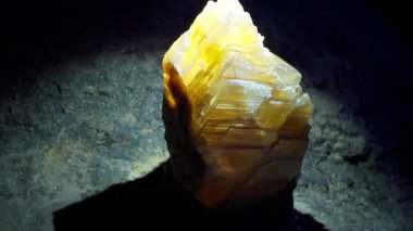Göz kamaştırıcı ve parlak sarı kristal bir oluşum karanlık bir mağara ortamında güzel bir parlaklık yayar.