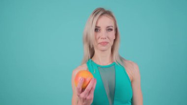 Bir fitness meraklısı kendinden emin bir şekilde parlak bir portakalla poz verir, sağlık, canlılık ve refahı teşvik eder.