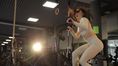 Kararlı bir kadın modern bir spor salonunda sabit bir bisiklete biniyor. Forma olan bağlılığını gösteriyor.