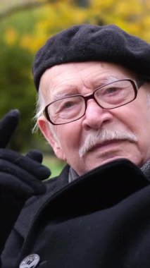 Bere ve şık gözlüklerle süslenmiş yaşlı bir adam, doğanın tadını çıkarırken düşünceli bir şekilde poz veriyor.