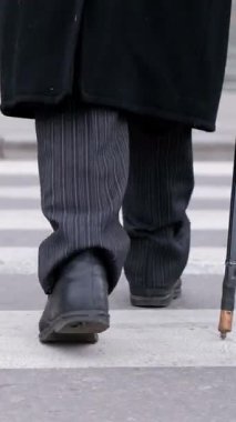 Şık ve ince çizgili pantolon giymiş yaşlı bir adam karşıdan karşıya geçerken bastonla zarif bir şekilde yürür.