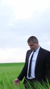 Resmi takım elbiseli bir işadamı bulutlu bir gökyüzünün altında canlı yeşil bir tarım alanını yakından izliyor.