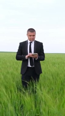 Sivri takım elbiseli bir işadamı, akıllı telefonuyla meşgul, yemyeşil bir alanda yürüyor..