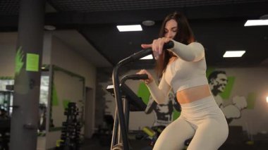 Modern spor salonunda eliptik eğitmen üzerine yoğun bir şekilde çalışan atletik ve formda bir kadın..