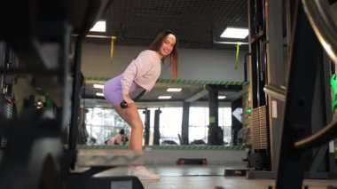 Spor salonunda egzersiz makinesinin üzerinde çeşitli dambıllarla çalışan atletik bir kadın..