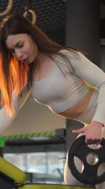 Formda bir kadın ağırlık kaldırırken güçlü ve dikkatlidir. Dikey video.