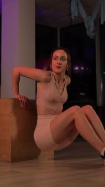 Genç bir kadın, parlak neon ışıklarla aydınlatılmış çağdaş bir spor salonunda bacak egzersizleri yapıyor. Dikey video.