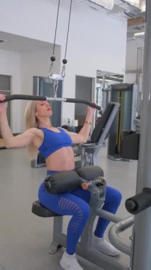 Güç antrenmanına odaklanmış spor salonunda formda ve kendini işine adamış bir kadın. Dikey video.