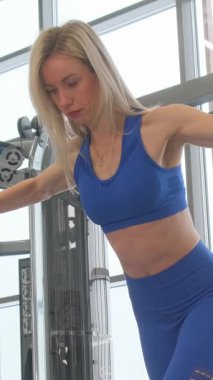 Modern bir spor salonunda direniş bantlarıyla egzersiz yapan bir kadın. Dikey video.