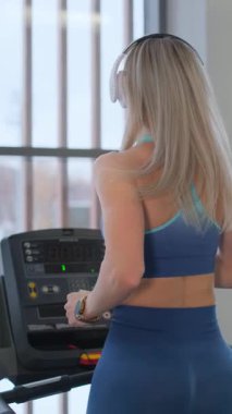 Modern bir spor salonundaki koşu bandında koşan odaklanmış bir sporcu, spora olan bağlılığını gösteriyor. Dikey video.