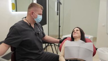 Arkadaş canlısı bir dişçi, modern bir diş sağlığı kliniğinde konfor ve kaliteli bakım için tasarlanmış bir hastayla sohbet ediyor..