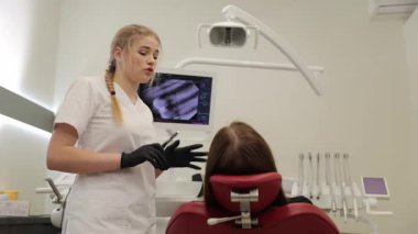 Modern bir klinikte, bir dişçi hastasıyla çeşitli tedavi seçeneklerini tartışır..