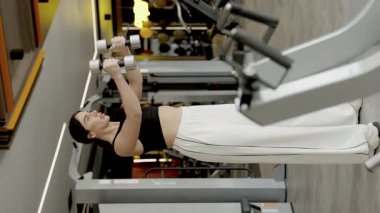 Çağdaş bir spor salonunda dambıllarla egzersiz yapan bir kadın dayanıklılık ve zindelik gösterir..