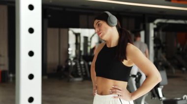 Odaklanmış bir kadın spor salonunda esniyor, kulaklıkla müzik dinliyor ve spor yapıyor.