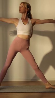 Evde yoga yapan sportif bir kadın, sağlıklı bir yaşam tarzını teşvik ediyor. Dikey video.