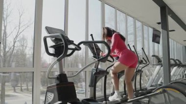 Kendine güvenen bir kadın, eliptik bir spor salonunda, sağlık ve sağlığa odaklı, modern bir spor salonunda çalışıyor.