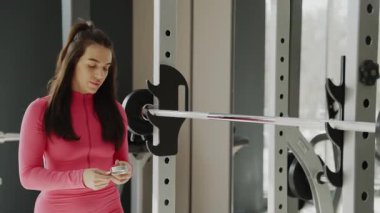 Parlak pembe kıyafetli kendini işine adamış bir bayan sporcu yoğun bir şekilde modern bir spor salonundaki antrenmanına odaklanmış durumda.