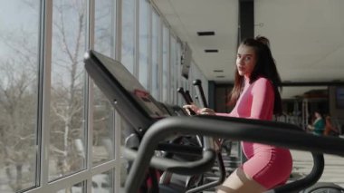 Spor salonunda eliptik bir eğitmen üzerinde egzersiz yapan bir kadın sağlık, sağlık ve refahı geliştiriyor..