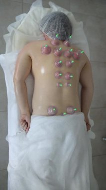 Klinikteki terapi seansı sırasında sırtında elektrikli süpürgelerle masaj yatağında uzanan rahat bir kadın. Dikey video