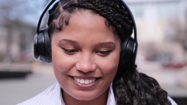 Şık kulaklıklar takan Afrikalı bir Amerikalı kadın, tamamen müziğe dalmış, güneşli bir arka planda.