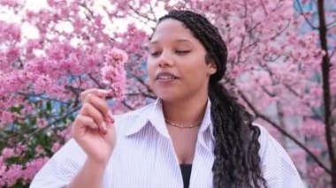 Afrikalı Amerikalı kadın, bahar aylarında canlı ve çarpıcı pembe kiraz çiçekleriyle çevrili doğanın güzelliğini neşeyle kucaklıyor.. 