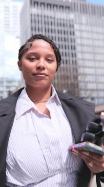 Kendine güvenen Afrikalı Amerikalı iş kadını şehir ortamında telefonu tutuyor, modern profesyonelliği somutlaştırıyor..