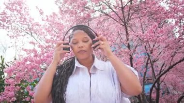 Baharda çiçek açan kiraz ağaçlarının canlı güzelliğiyle çevrili Afro-Amerikan kadın farkındalık meditasyonuna girişiyor..