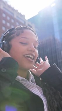 Neşeli genç Afrikalı Amerikalı kadın neşeli bir şehir ortamında açık havada müziğinin keyfini çıkarıyor..