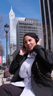 Genç bir Afrikalı Amerikalı kadın açık havada canlı bir şehir ortamında müzik dinlemekten keyif alıyor, kendine güven ve neşe saçıyor..