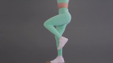 Zayıf vücutlu bir kadın gri arka planda topla çömelme hareketleri yapıyor. Ek ekipmanlarla aktif fitness egzersizi