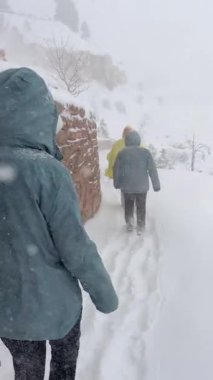 Yürüyüş arkadaşları, şiddetli bir kış fırtınası sırasında karlı bir patikada yürürler. Bu, dayanıklılıklarını ve maceracı ruhlarını gösterir.