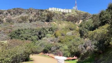Güneşli bir günde yürüyüş yapan bir adam Hollywood tabelasının nefes kesici manzarasından mutlu bir şekilde zevk alır..